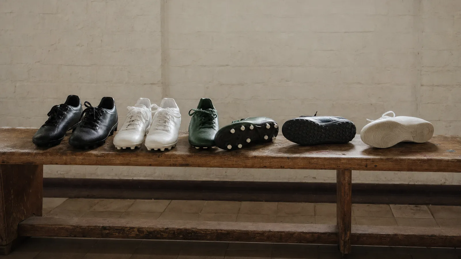 Mehrere Paar Kinder-Fußballschuhe mit unterschiedlichen Sohlen – von Nocken bis Hallensohle – stehen auf einer Holzbank in der Kabine.